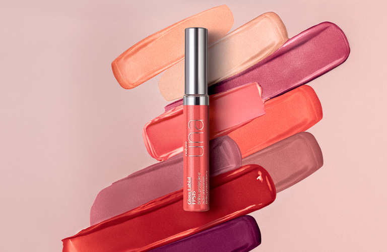 Na imagem temos um gloss labial, e ao fundo algumas texturas das demais cores do mesmo produto.